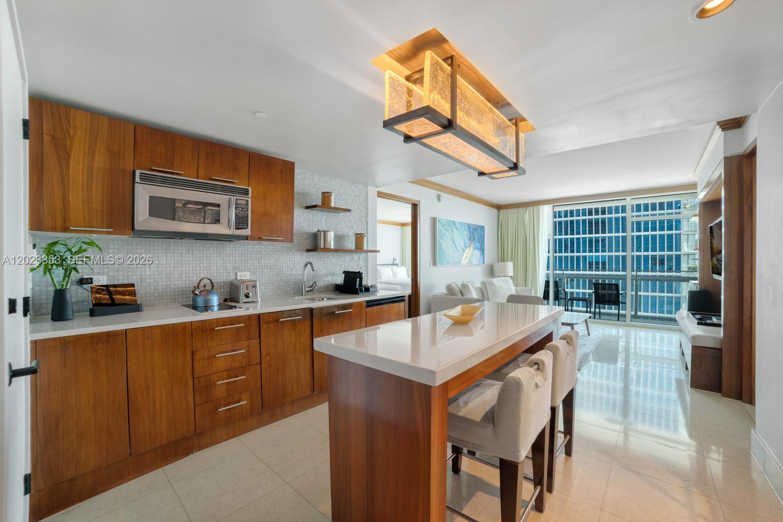 A modern kitchen features wood cabinetry, a quartz island, and a dining area with balcony access — 6801 Collins Ave, Miami Beach FL 33141, MIAMI BEACH, FL