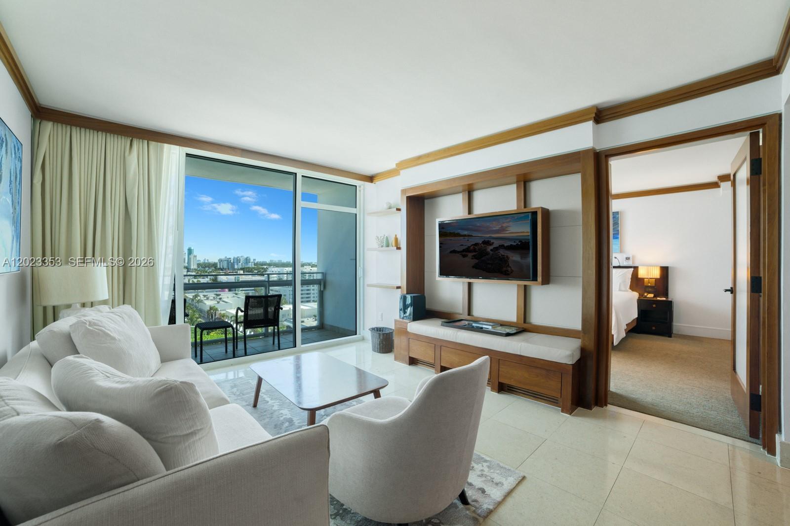 A living room features a white sofa, a television unit, and a balcony with city views — 6801 Collins Ave, Miami Beach FL 33141, MIAMI BEACH, FL