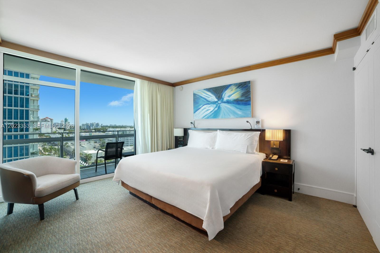 A hotel bedroom features a king bed, a balcony with city views, and modern decor — 6801 Collins Ave, Miami Beach FL 33141, MIAMI BEACH, FL
