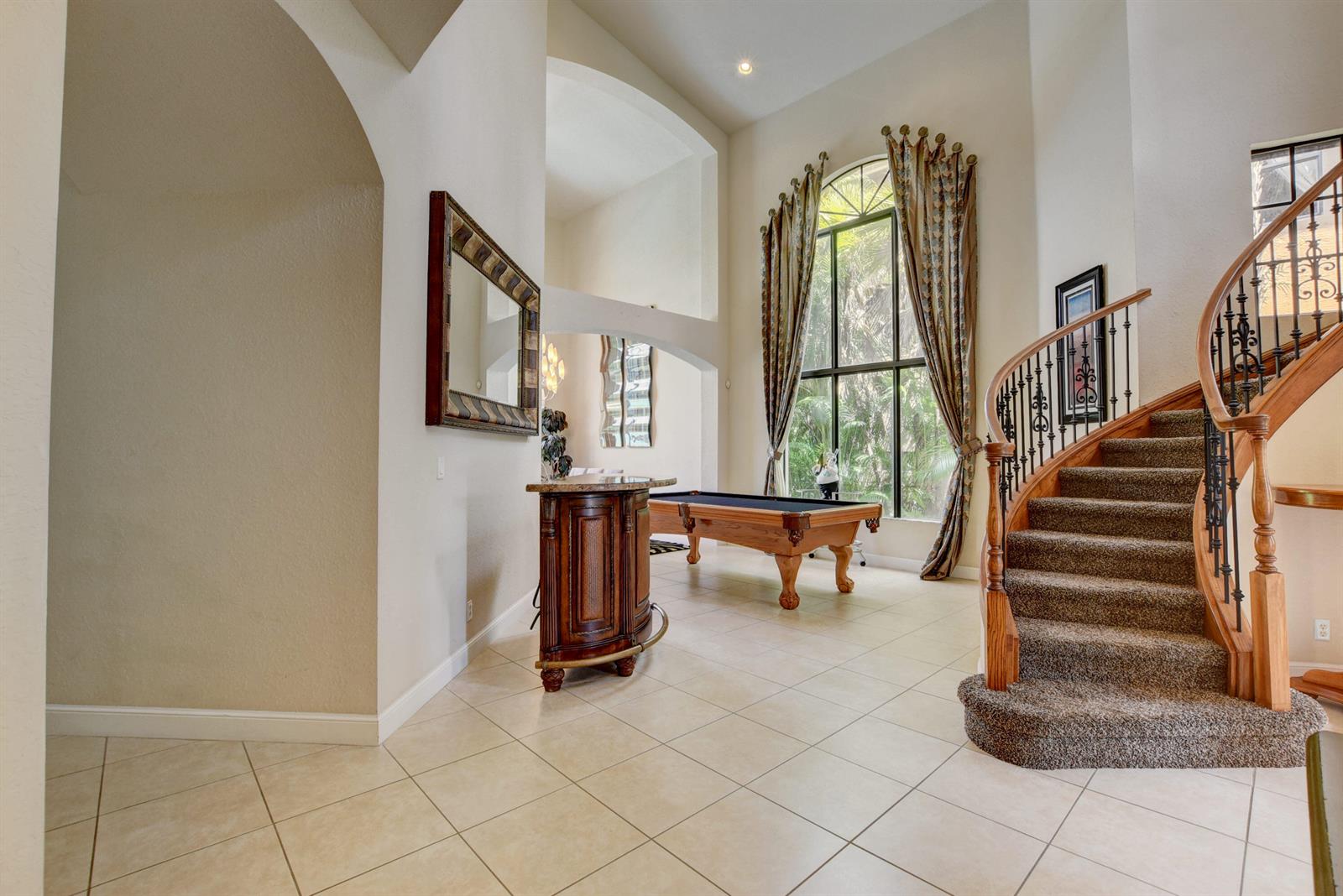 A foyer with a curved staircase, tile flooring, and a pool table near a large window — 3424 Collonade Drive, Wellington FL 33449, WELLINGTON, FL