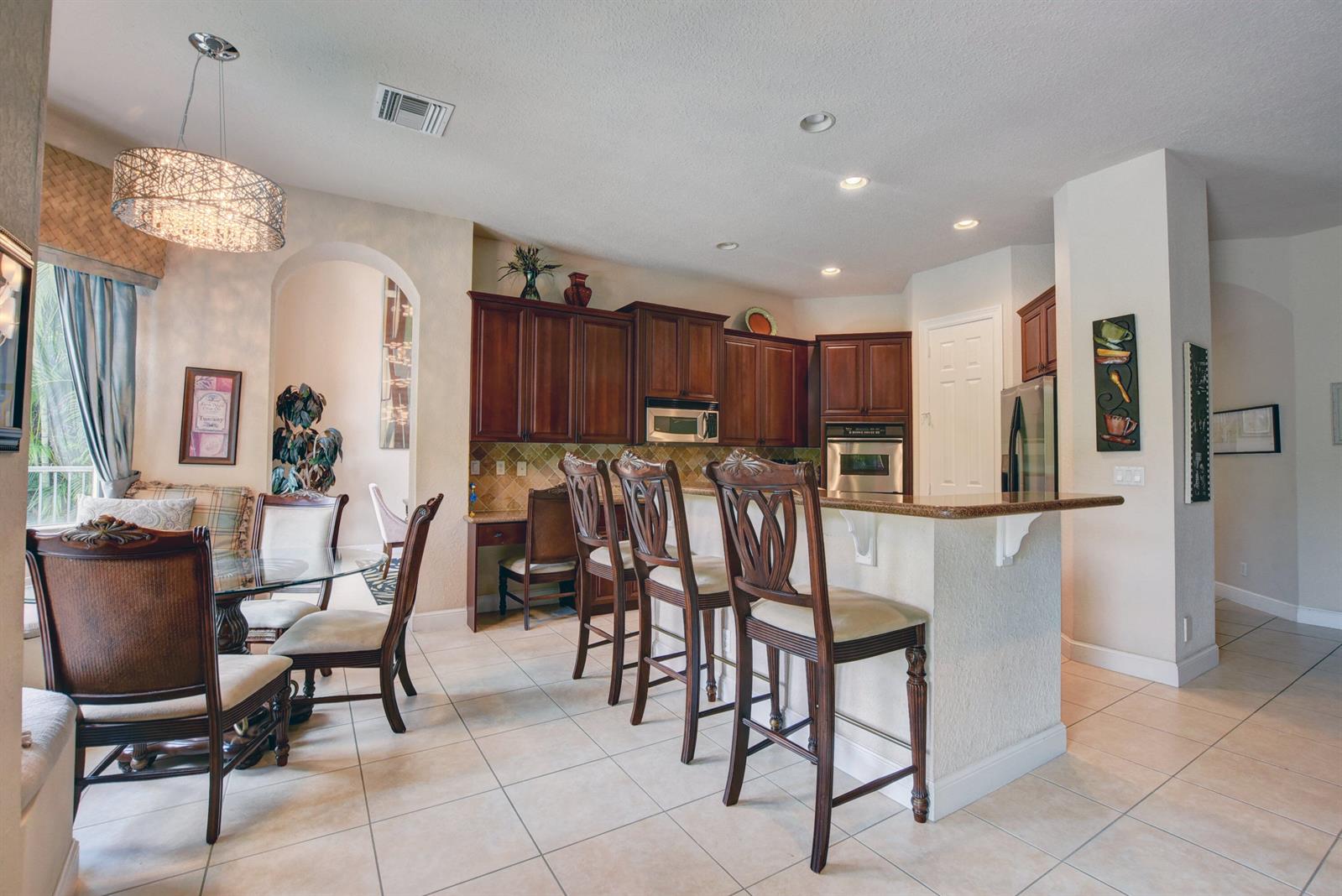A kitchen with dark wood cabinets, a granite breakfast bar, and an adjacent dining area — 3424 Collonade Drive, Wellington FL 33449, WELLINGTON, FL