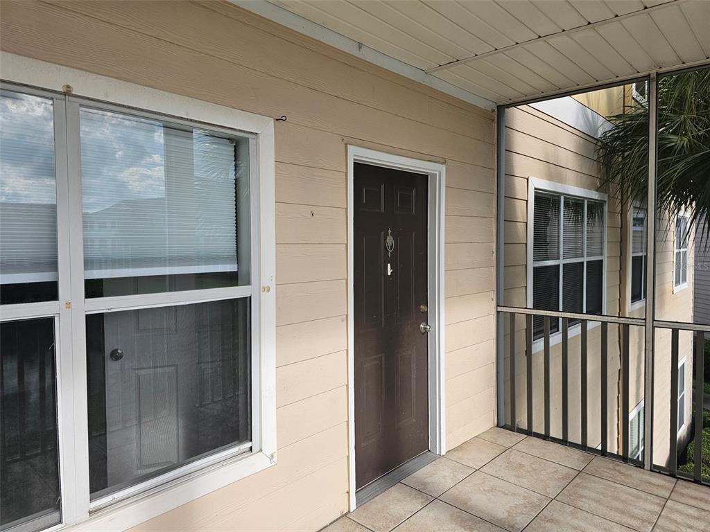 A brown entry door is centered on a covered balcony with tiled flooring and windows — 4802 51ST STREET W UNIT 1610, BRADENTON, FL