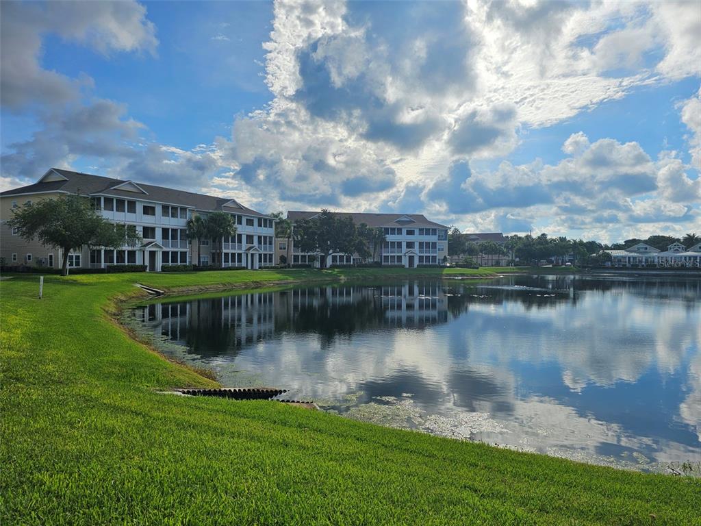A multi-story apartment building sits beside a pond under a cloudy blue sky — 4802 51ST STREET W UNIT 1610, BRADENTON, FL