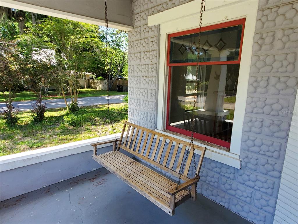 A wooden porch swing hangs on a covered porch with patterned stone siding — 23882 NW 187TH AVENUE, HIGH SPRINGS, FL
