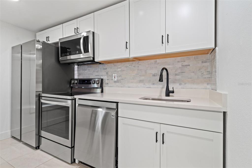 A kitchen features white cabinets, stainless steel appliances, a tiled backsplash, and a black faucet — 609 N OSCEOLA AVENUE UNIT A & B, CLEARWATER, FL