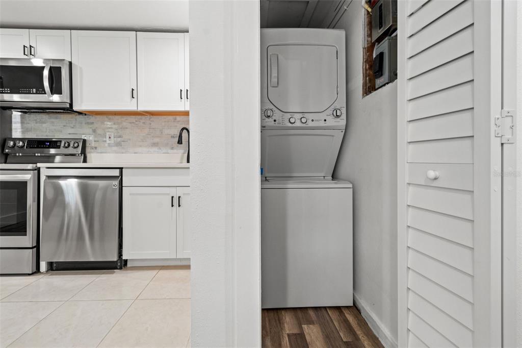 A kitchen with white cabinets and stainless steel appliances sits next to a stacked laundry unit — 609 N OSCEOLA AVENUE UNIT A & B, CLEARWATER, FL