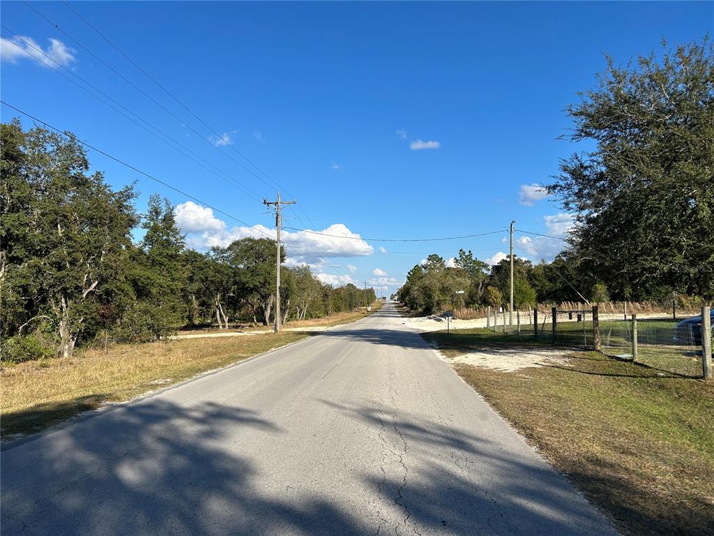 A paved road stretches into the distance between wooded areas under a clear blue sky — TBD NE 69TH LANE, WILLISTON, FL