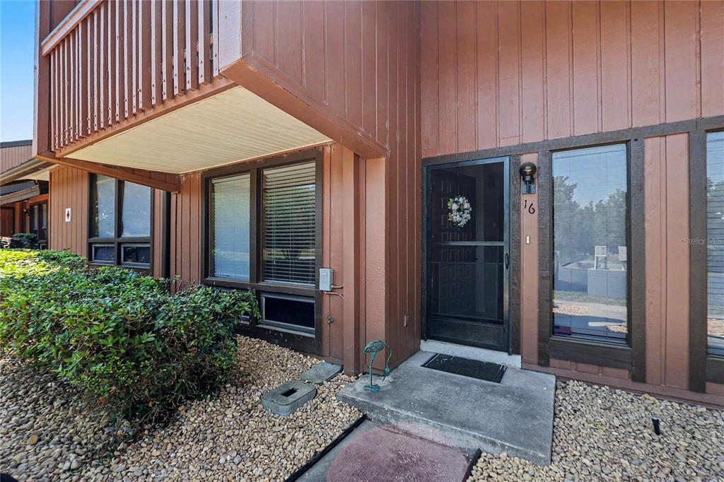 The exterior of a brown wood-sided townhouse features a front door with a screen — 19660 SW 83RD PLACE ROAD UNIT C16, DUNNELLON, FL