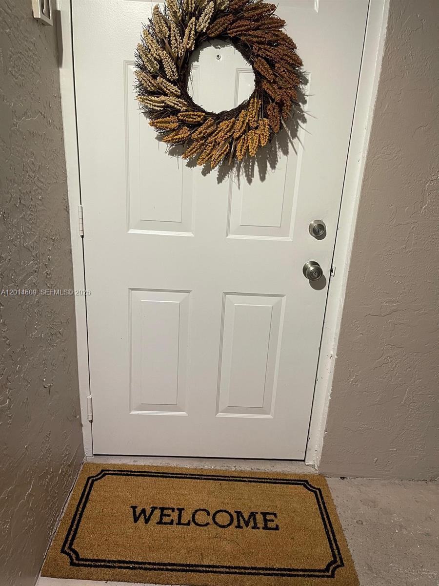 A white front door with a decorative wreath and a welcome mat on the floor — 17550 NW 67th Pl # 2, Hialeah FL 33015, HIALEAH, FL