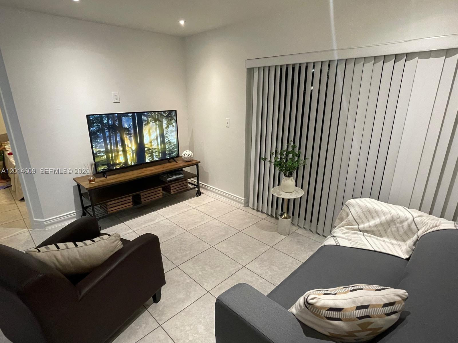 A living room features a television on a media console, a sofa, and vertical blinds — 17550 NW 67th Pl # 2, Hialeah FL 33015, HIALEAH, FL