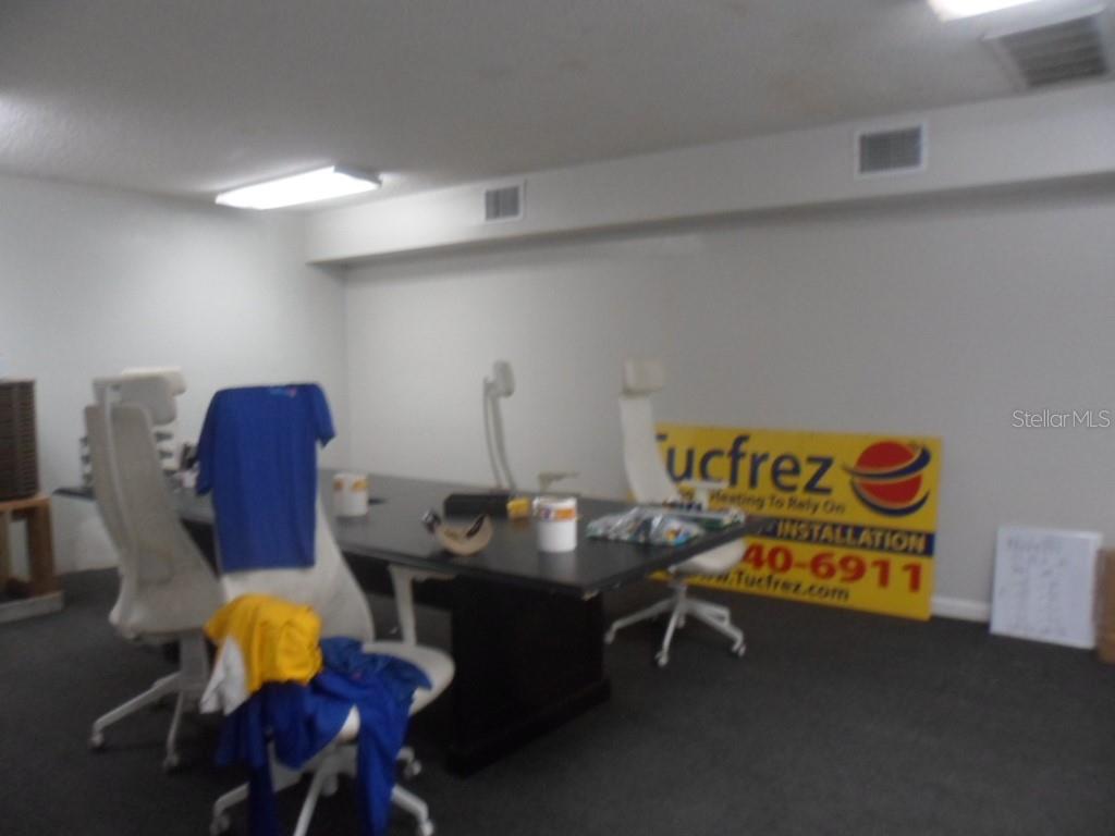 An office room features a large conference table, several chairs, and a branded yellow sign — 1523-1525 KELLEY AVENUE, KISSIMMEE, FL