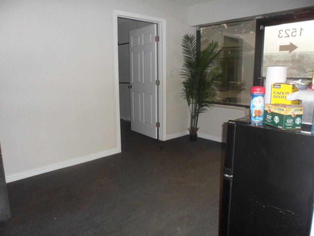 A room with dark carpet, a white door, a potted plant, and a refrigerator — 1523-1525 KELLEY AVENUE, KISSIMMEE, FL