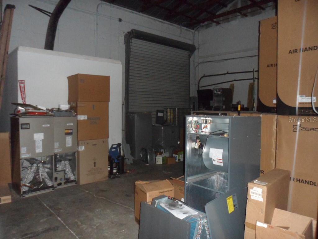 A warehouse interior features HVAC equipment, cardboard boxes, and a large metal roll-up door — 1523-1525 KELLEY AVENUE, KISSIMMEE, FL