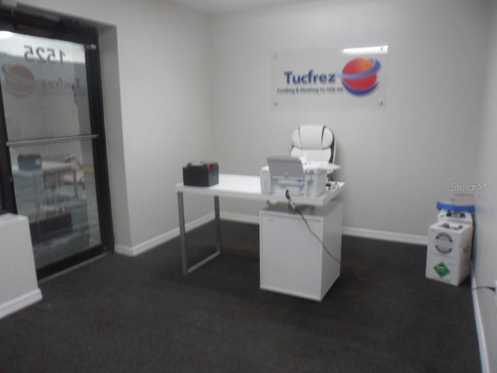 A small office space features a white desk, a chair, and a company logo sign — 1523-1525 KELLEY AVENUE, KISSIMMEE, FL