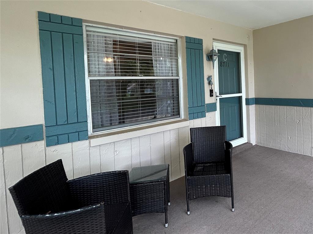 A covered porch features two black wicker chairs, a small table, and a teal door — 8711 SW 96TH LANE UNIT C, OCALA, FL