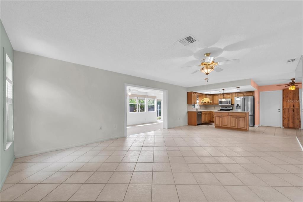 A spacious room with light tile flooring, a ceiling fan, and an open-concept kitchen — 12939 115TH STREET, LARGO, FL