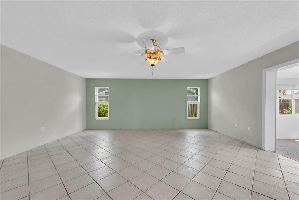 An empty room features light-colored tile flooring, a sage green accent wall, and a ceiling fan — 12939 115TH STREET, LARGO, FL