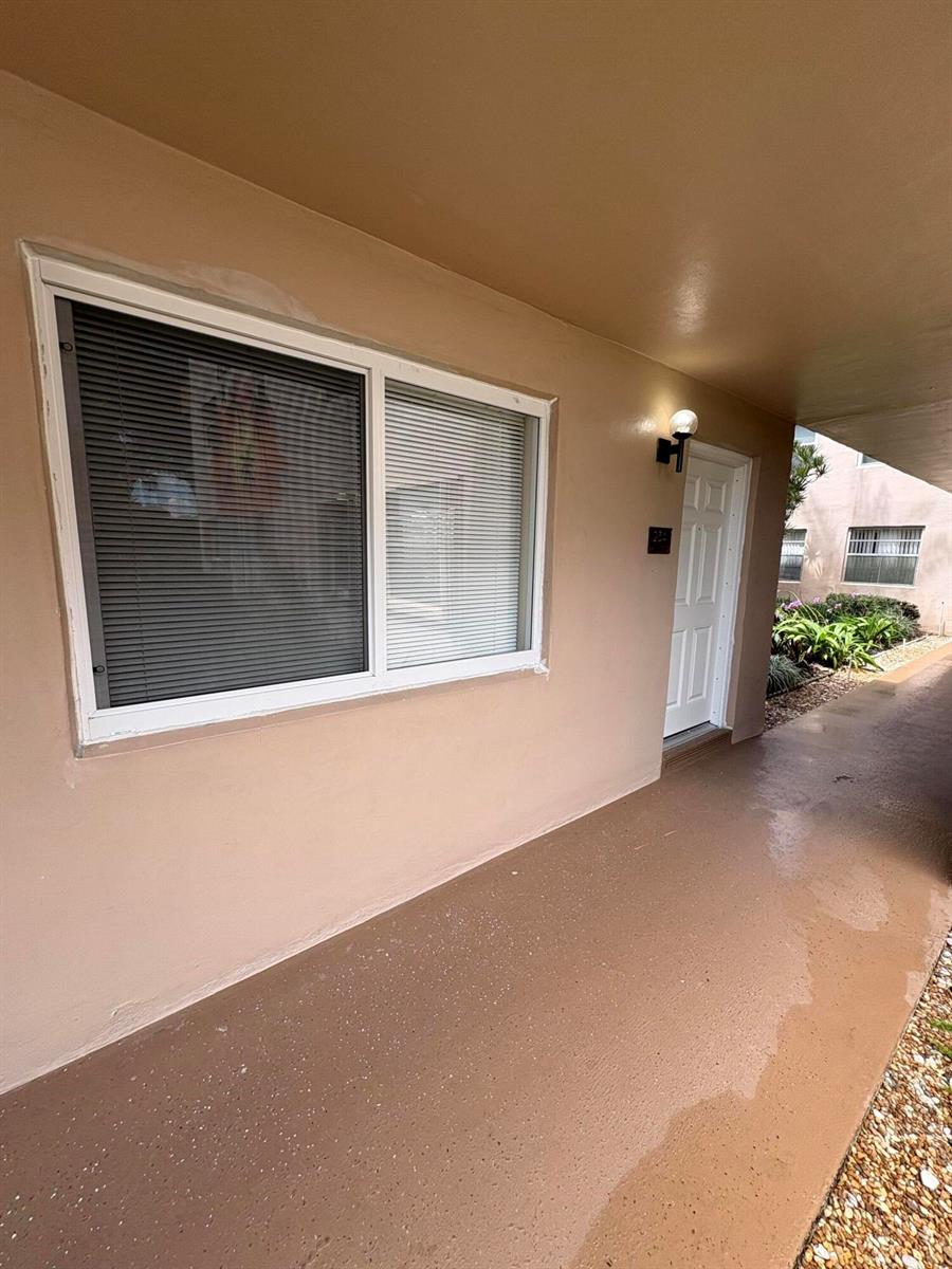 A tan exterior walkway leads to a white front door next to a sliding window — 23 Flanders A, Delray Beach FL 33484, DELRAY BEACH, FL