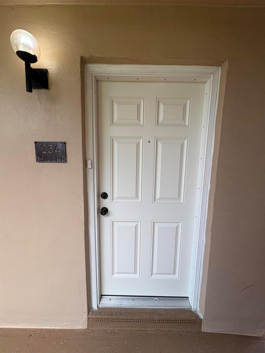 A white six-panel exterior door with a black handle and a wall-mounted address plaque — 23 Flanders A, Delray Beach FL 33484, DELRAY BEACH, FL