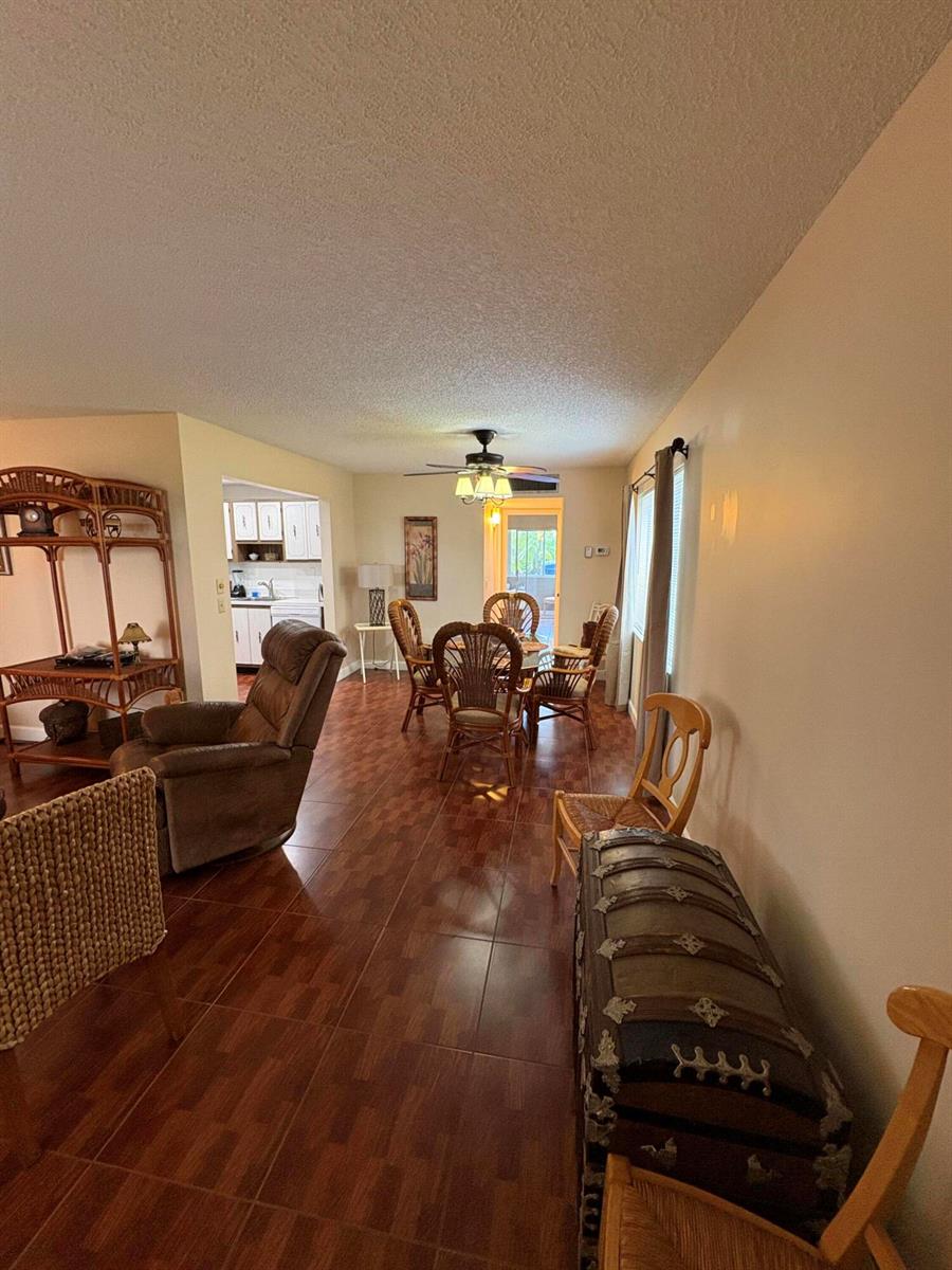 A living and dining area with tiled floors, wicker furniture, and a ceiling fan — 23 Flanders A, Delray Beach FL 33484, DELRAY BEACH, FL