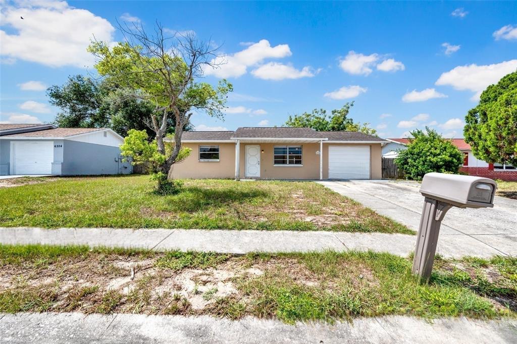 A single-story house with a tan exterior, a white front door, and an attached garage — 6318 BALDWYN AVENUE, NEW PORT RICHEY, FL