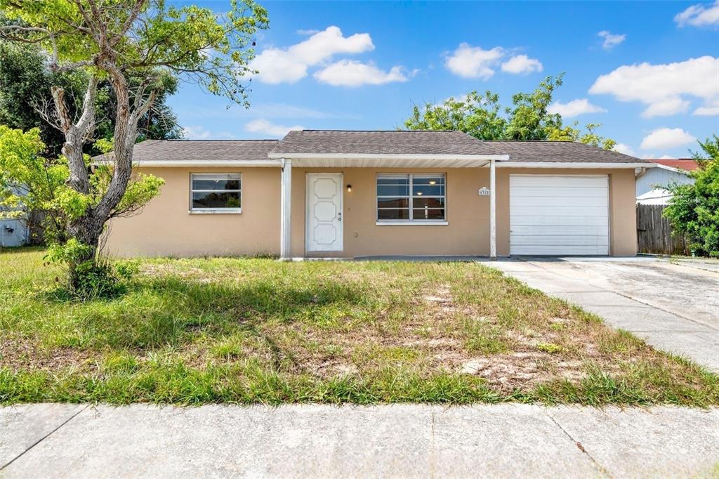 A single-story tan house with a white front door, a garage, and a front lawn — 6318 BALDWYN AVENUE, NEW PORT RICHEY, FL