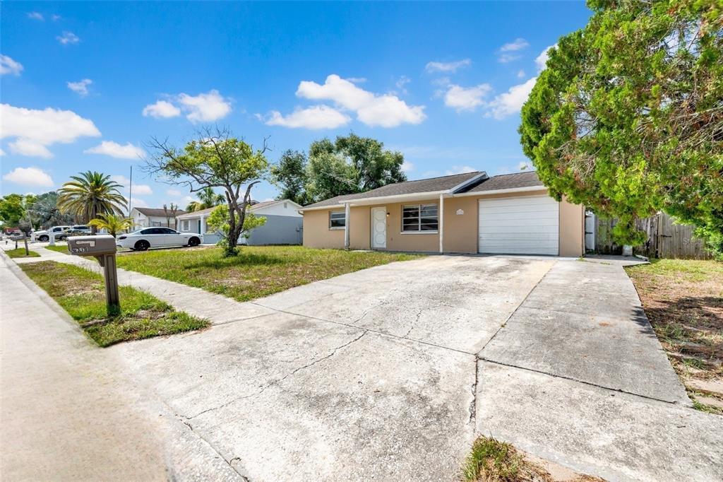 A single-story house with a tan exterior, white garage door, and a concrete driveway — 6318 BALDWYN AVENUE, NEW PORT RICHEY, FL