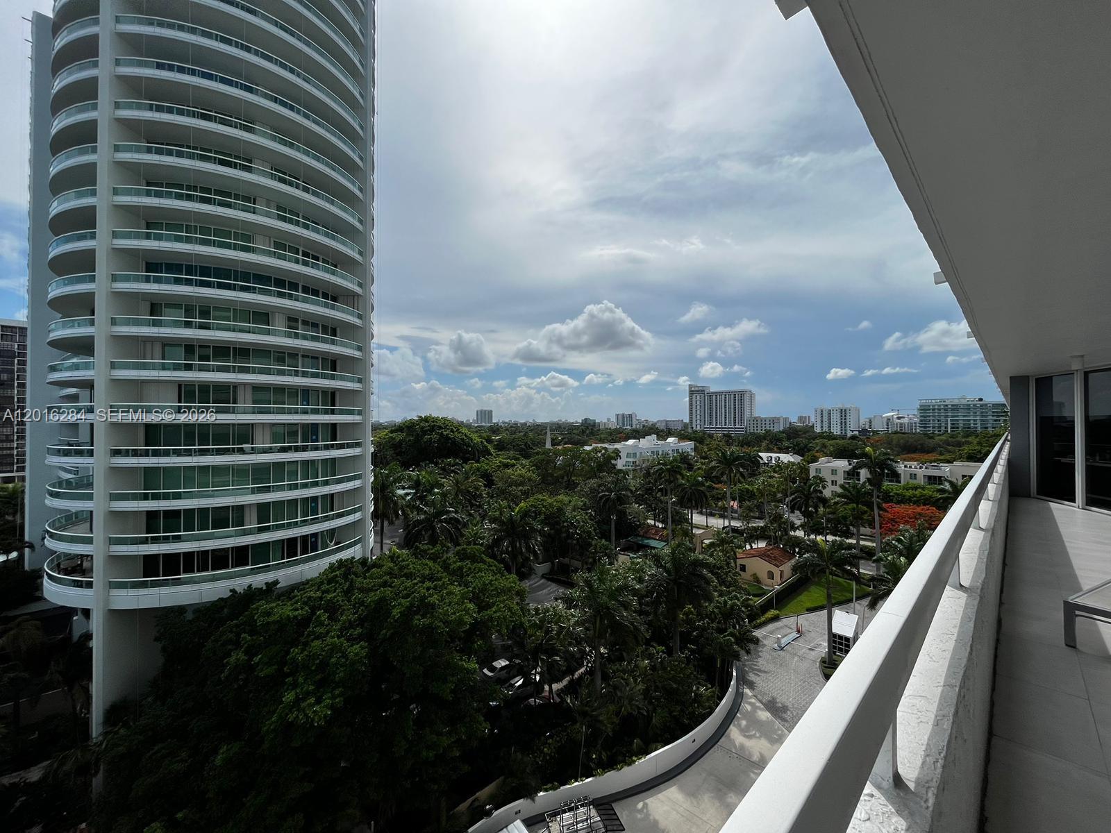 A balcony view overlooks a lush green landscape and a tall, cylindrical residential building — 1627 Brickell Ave # 1204, Miami FL 33129, MIAMI, FL