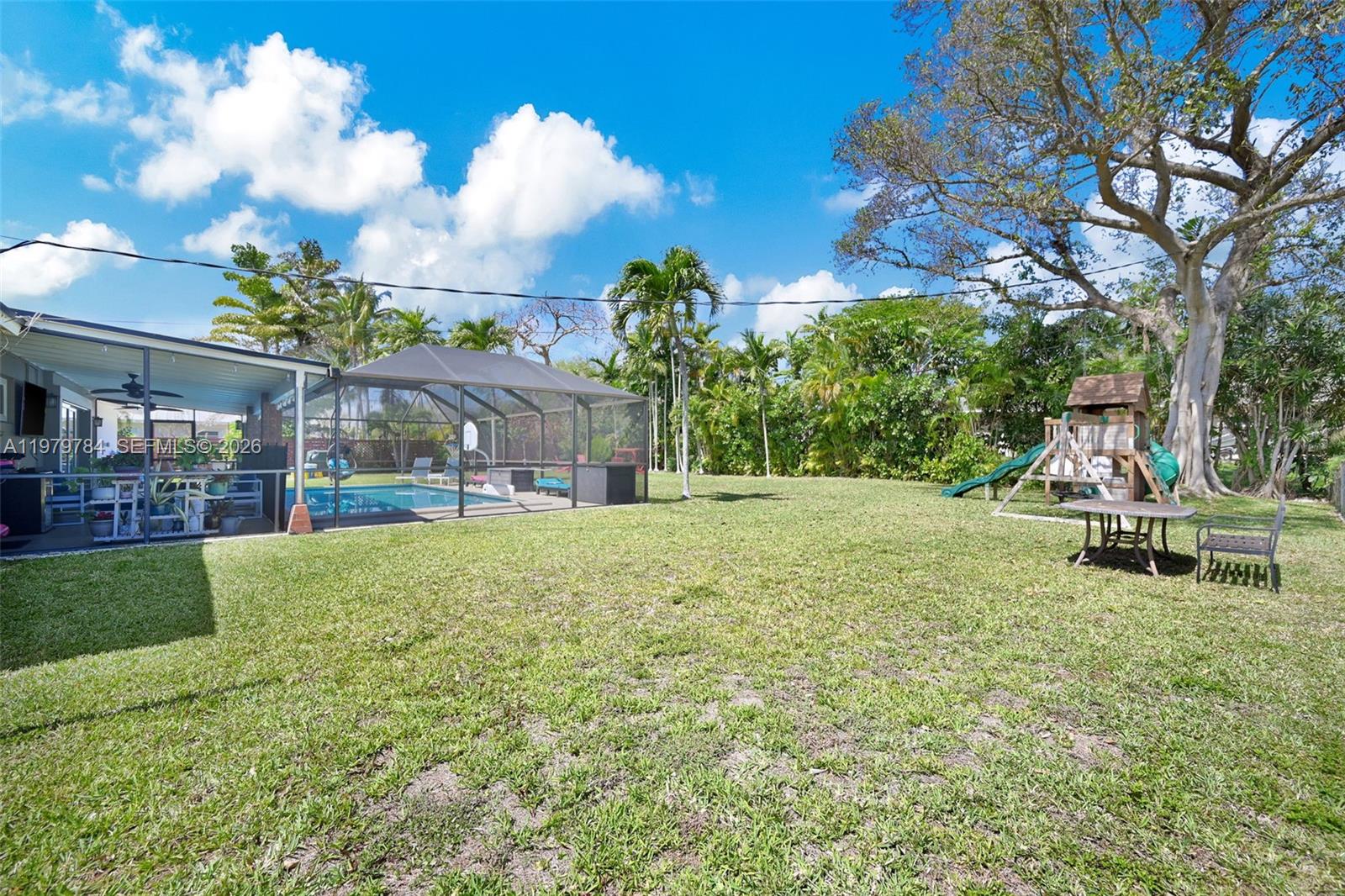 A backyard features a screened-in pool, a wooden playset, and a patio table on grass — 8935 SW 186th Ter, Cutler Bay FL 33157, CUTLER BAY, FL