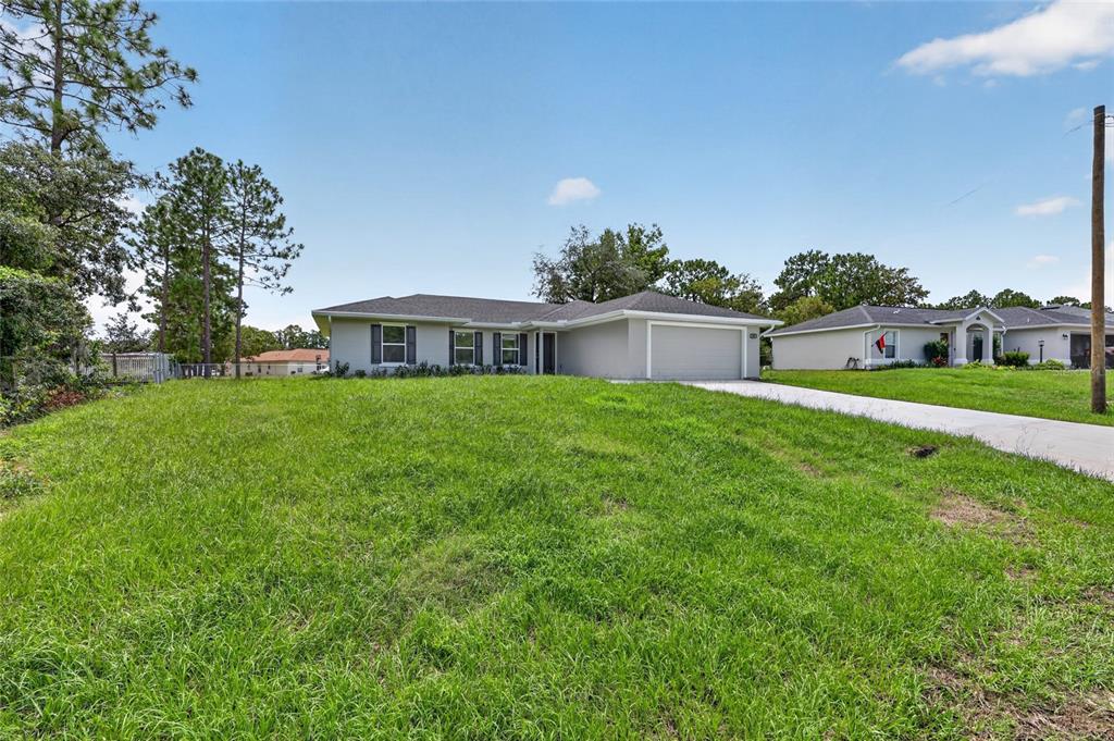A single-story house with a gray exterior, a two-car garage, and a large front lawn — 13 PECAN DRIVE LOOP, OCALA, FL