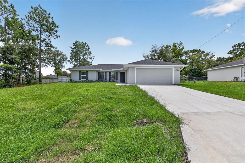 A single-story house with a gray exterior, a two-car garage, and a large front lawn — 13 PECAN DRIVE LOOP, OCALA, FL