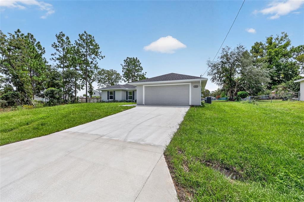 A single-story house with a gray garage and a concrete driveway sits on a lawn — 13 PECAN DRIVE LOOP, OCALA, FL