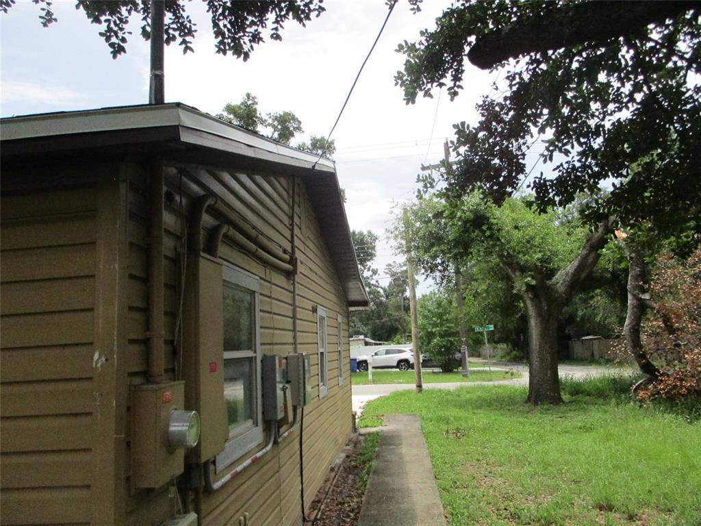 The exterior side of a tan house features a concrete walkway and electrical utility boxes — 302 E 130TH AVENUE, TAMPA, FL