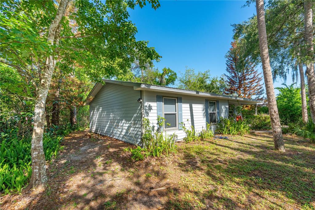 A single-story house with light gray siding sits in a wooded, grassy yard — 240 NEWCOMB STREET, NEW SMYRNA BEACH, FL