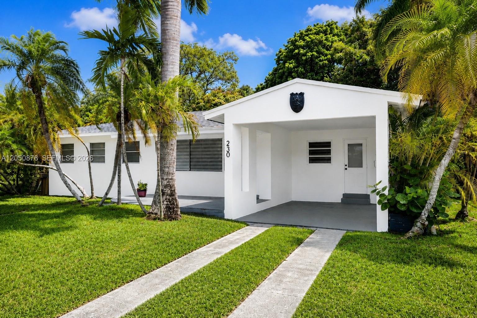 A white single-story house features a front carport, a concrete driveway, and surrounding palm trees — 230 NE 2nd Pl, Dania Beach FL 33004, DANIA BEACH, FL