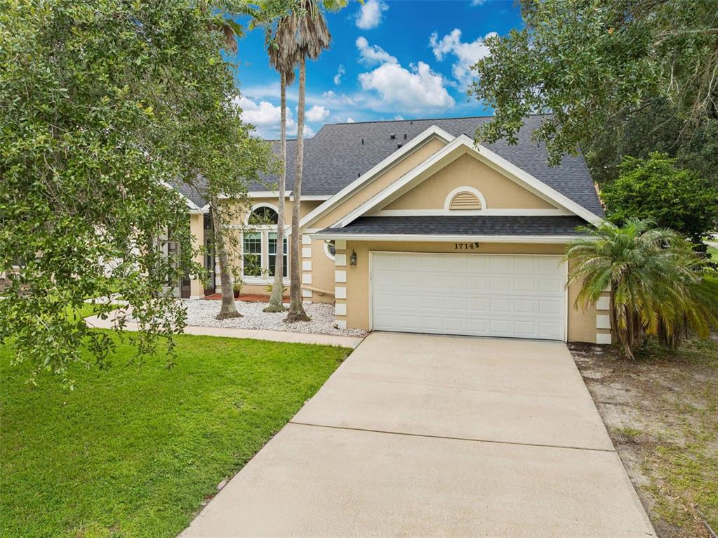 A tan single-story house with a white garage door, a concrete driveway, and palm trees — 1714 CYPRESS RIDGE DRIVE, ORLANDO, FL