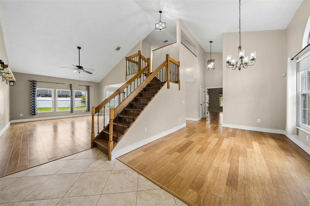 A foyer with wood flooring and a staircase leads to an open living area with vaulted ceilings — 1714 CYPRESS RIDGE DRIVE, ORLANDO, FL