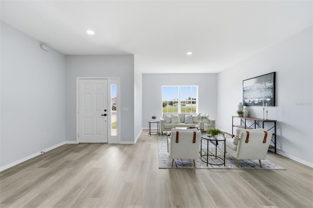 A bright living room features light wood-look flooring, white walls, and a large front window — 11661 SW 56TH TERRACE, OCALA, FL