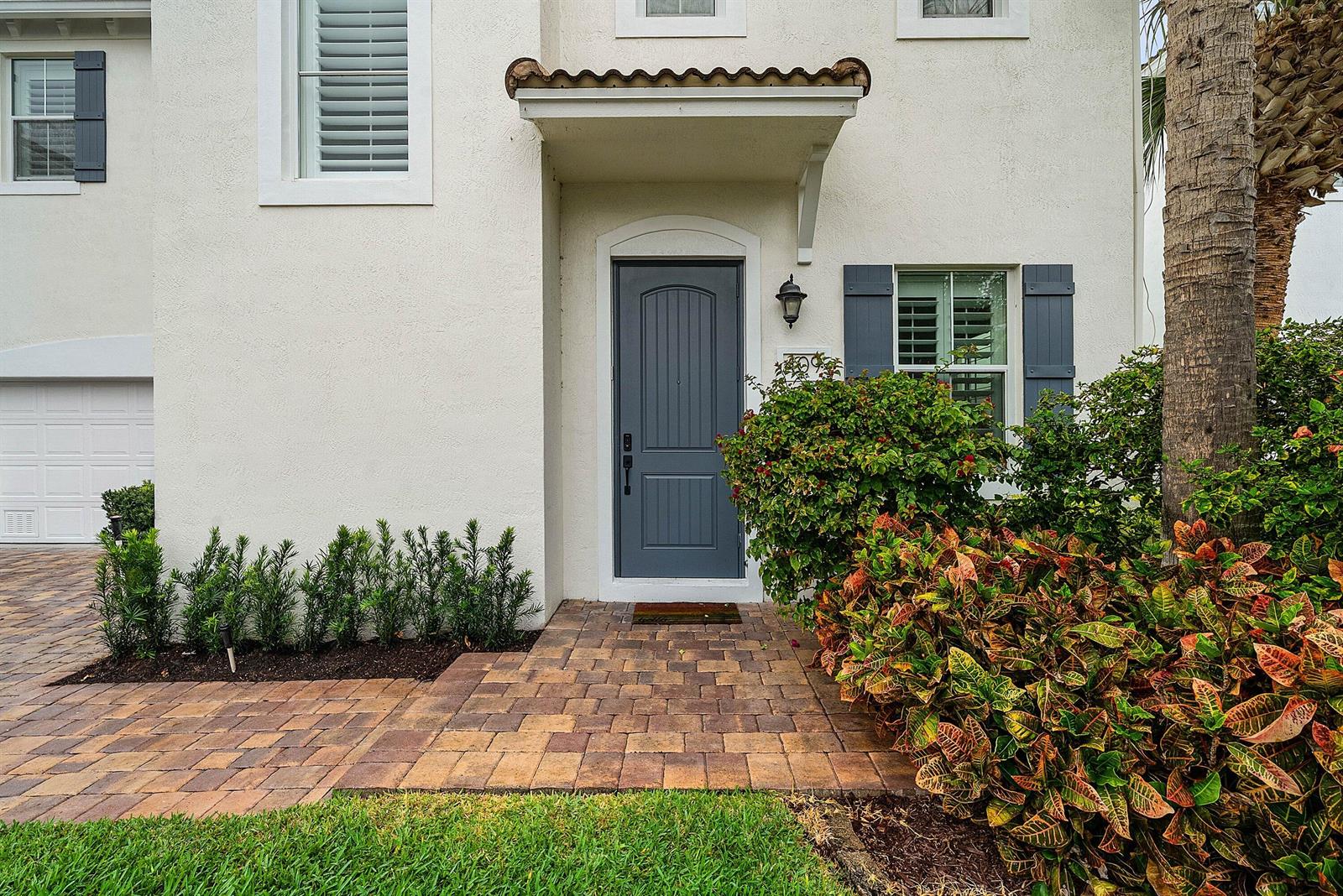 A front exterior view of a house with a gray door, paver walkway, and landscaping — 409 Francesca Ridge Road, Boynton Beach FL 33435, BOYNTON BEACH, FL