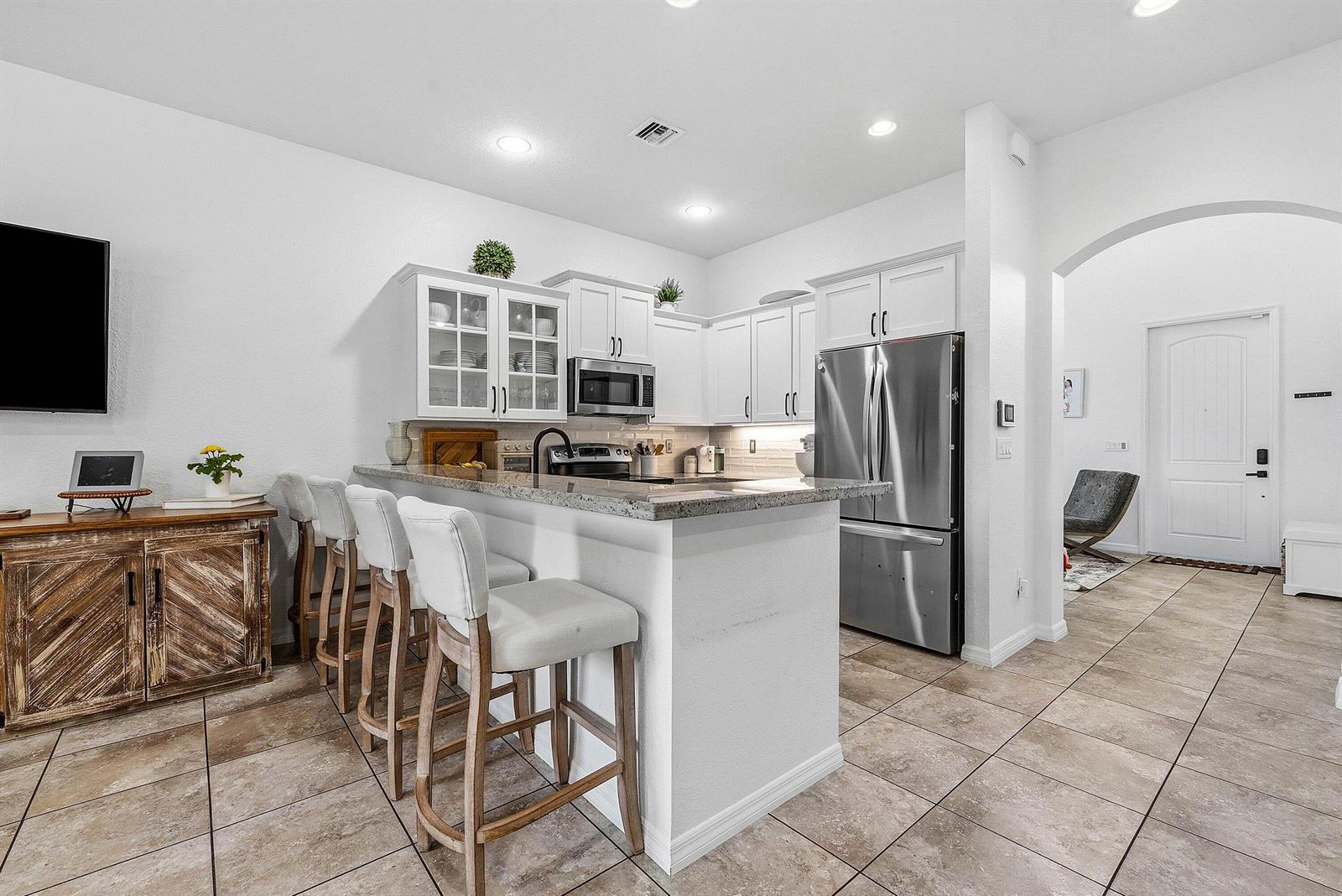 A kitchen features white cabinets, stainless steel appliances, a granite breakfast bar, and tile flooring — 409 Francesca Ridge Road, Boynton Beach FL 33435, BOYNTON BEACH, FL