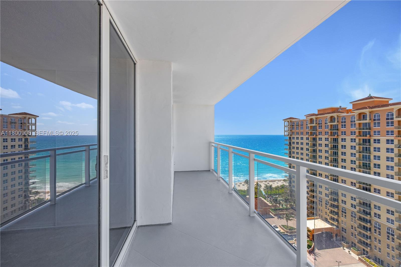 A balcony with glass railings overlooks the ocean and a neighboring high-rise building — 2030 S Ocean Dr # 1708, Hallandale Beach FL 33009, HALLANDALE BEACH, FL