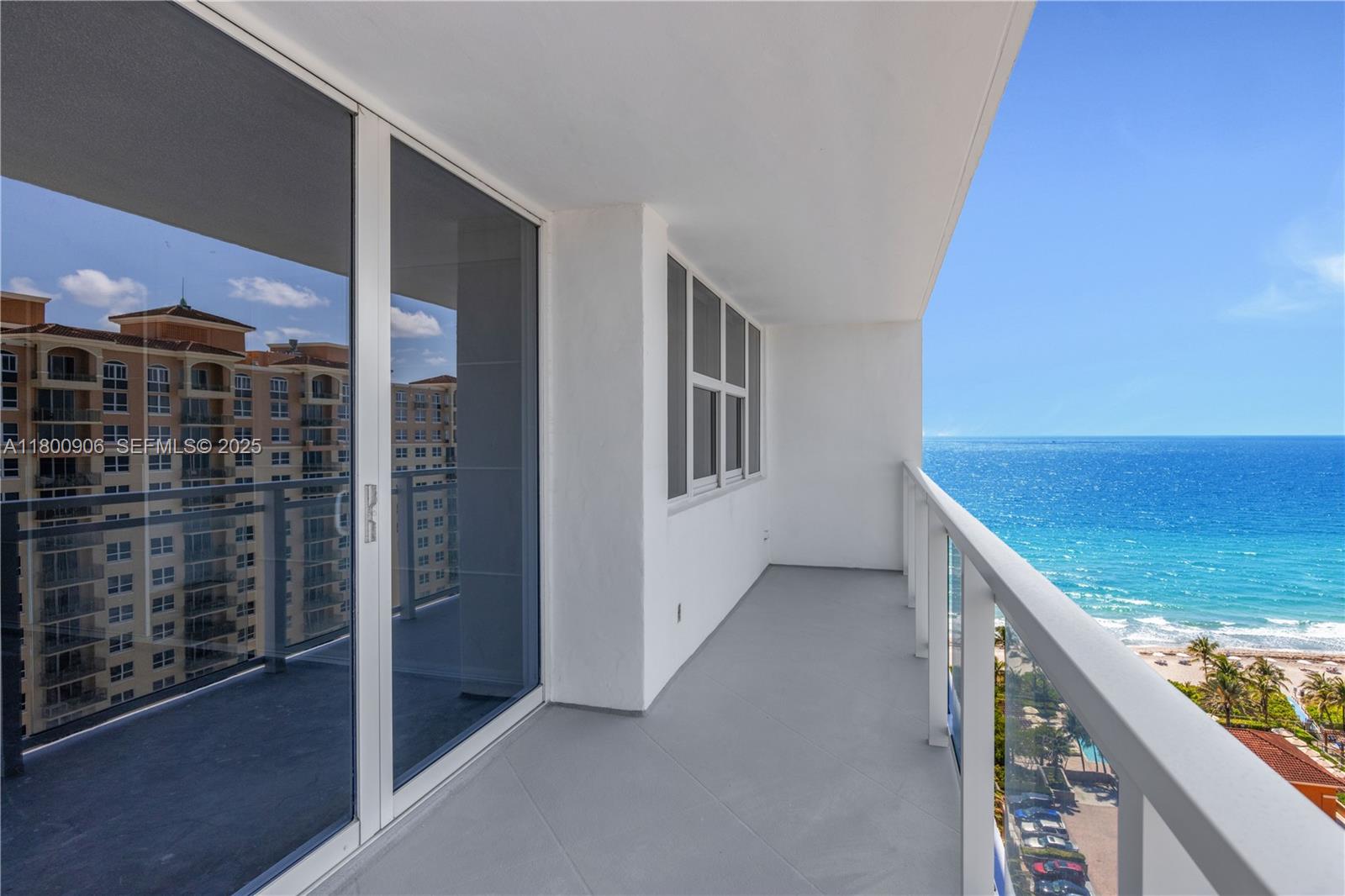 A balcony with a glass railing overlooks the ocean and a neighboring building — 2030 S Ocean Dr # 1708, Hallandale Beach FL 33009, HALLANDALE BEACH, FL