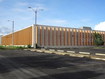 A large, rectangular commercial building with vertical orange fins stands beside an empty parking lot — Calle 2 PR-7731 INT PR 171, CIDRA, PR