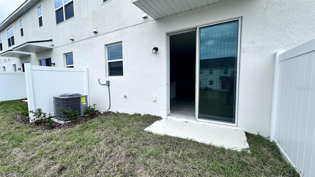The exterior of a townhouse features a sliding glass door, an AC unit, and fencing — 1167 BOARDWALK PLACE, KISSIMMEE, FL