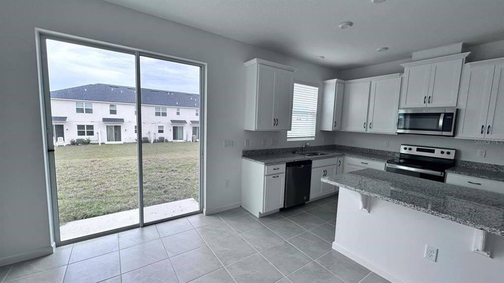 A kitchen with white cabinets, granite countertops, and a sliding glass door to the yard — 1167 BOARDWALK PLACE, KISSIMMEE, FL