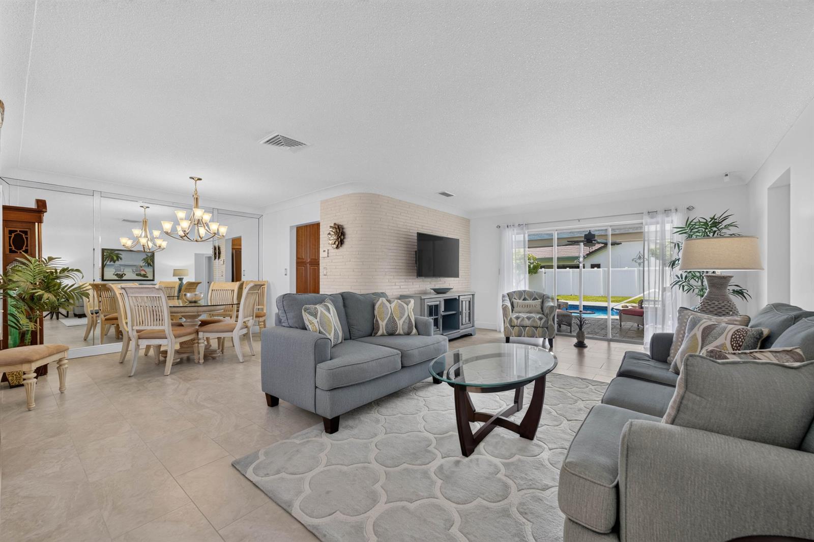 A living room with gray sofas, a glass coffee table, and a dining area nearby — 1517 SE 14TH Street, Deerfield Beach FL 33441, DEERFIELD BEACH, FL