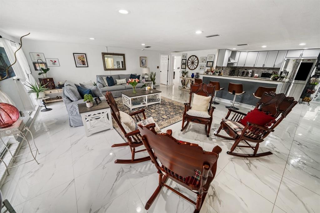 An open-concept living room and kitchen featuring white marble floors and wooden rocking chairs — 3549 ROCKAWAY DRIVE, HOLIDAY, FL