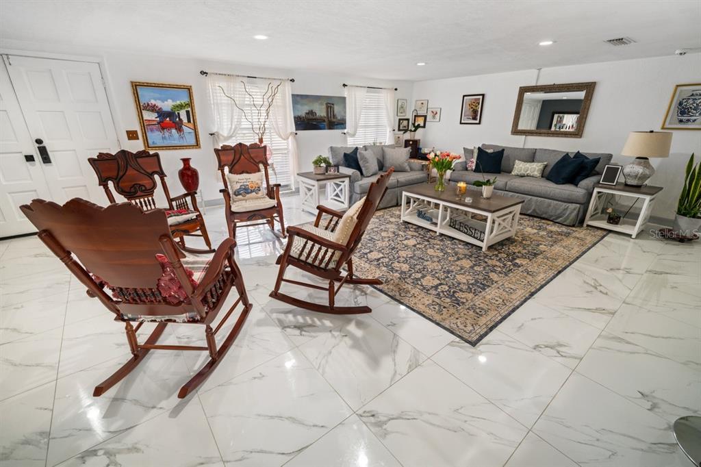 A living room features white marble-look tile floors, rocking chairs, and gray upholstered sofas — 3549 ROCKAWAY DRIVE, HOLIDAY, FL
