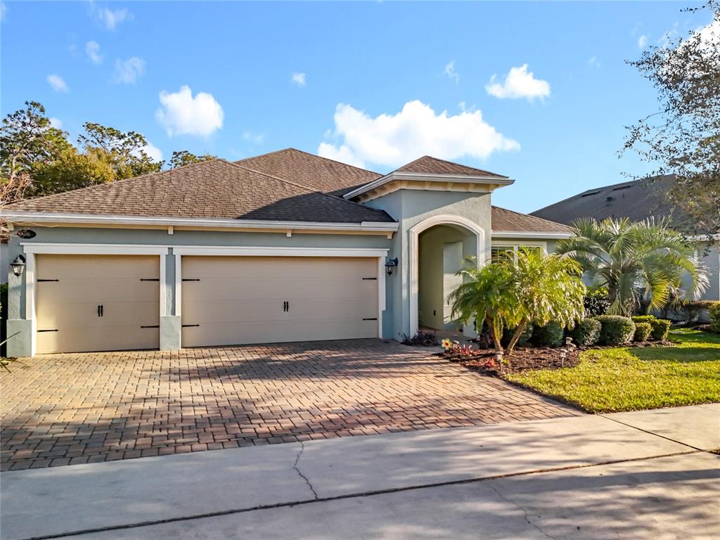 A single-story house with a three-car garage, paver driveway, and arched entryway under a blue sky — 295 NORTHCOTE COURT, DELAND, FL