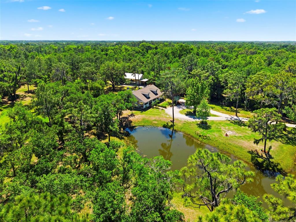 An aerial view shows a house and detached garage surrounded by trees and a pond — 1115 410TH COURT E, MYAKKA CITY, FL